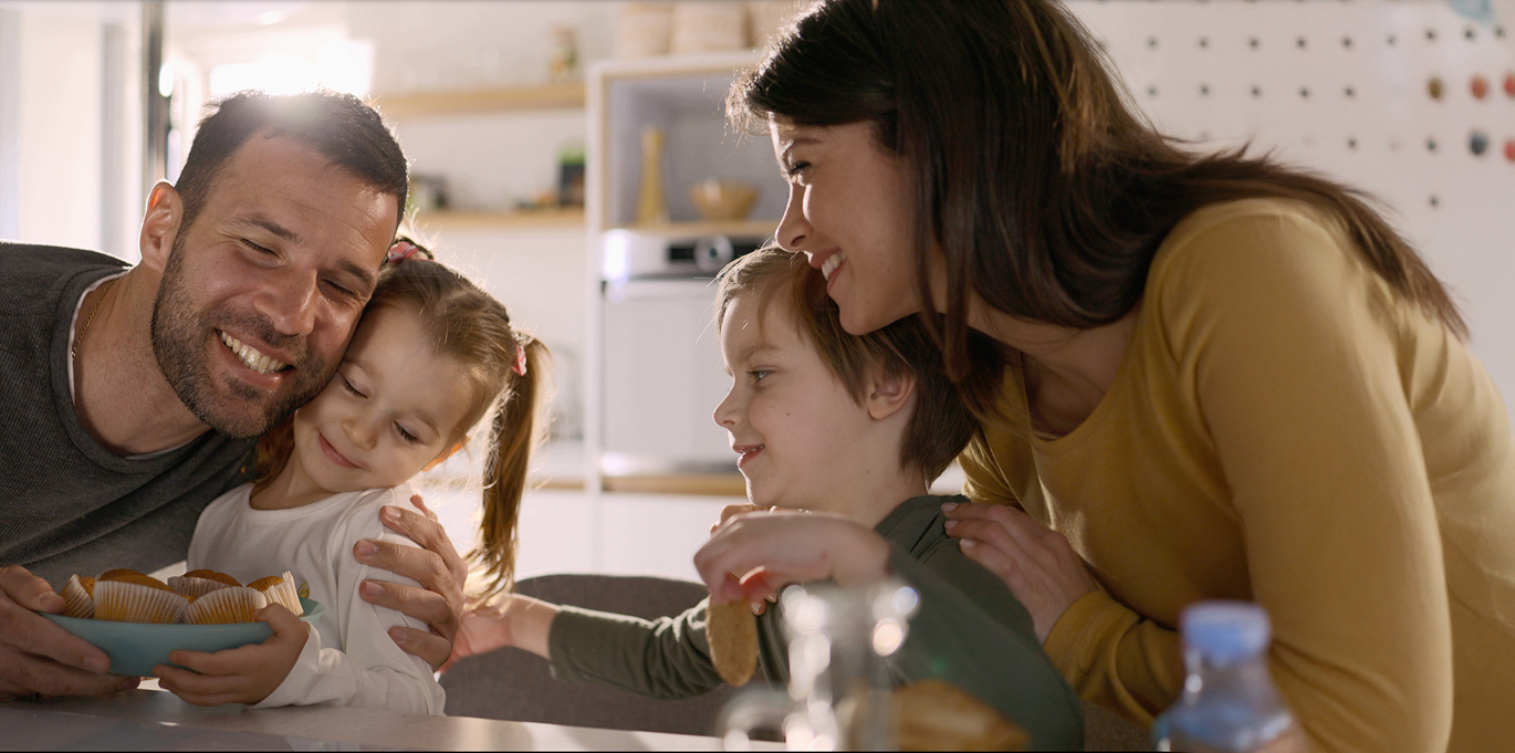 Χαρούμενη οικογένεια τρώει στην κουζίνα του σπιτιού της που είναι εξοπλισμένη με οικιακές μικροσυσκευές.