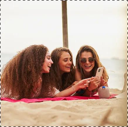 Τρείς γυναίκες στην παραλία, κοιτάζουν ένα smartphone και γελάνε