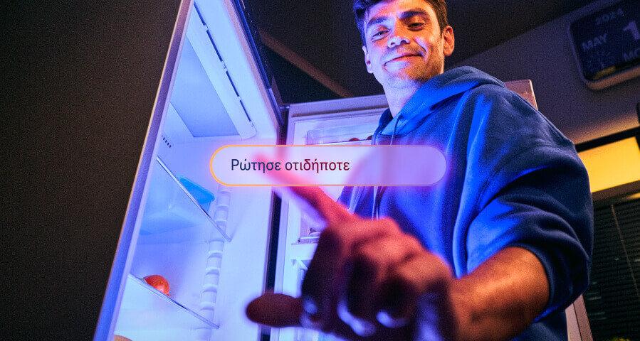 Άντρας με μπλε φούτερ στέκεται μπροστά σε ένα ανοιχτό ψυγείο τη νύχτα, χαμογελάει και δείχνει προς την κάμερα. Μπροστά του, ένα κουμπί αναγράφει «Ρώτησε οτιδήποτε».