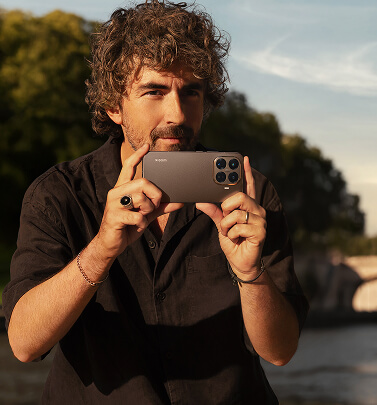 Ένας άντρας κρατάει το Xiaomi 15T Pro 5G οριζόντια, σαν να ετοιμάζεται να τραβήξει μια φωτογραφία σε εξωτερικό χώρο.
