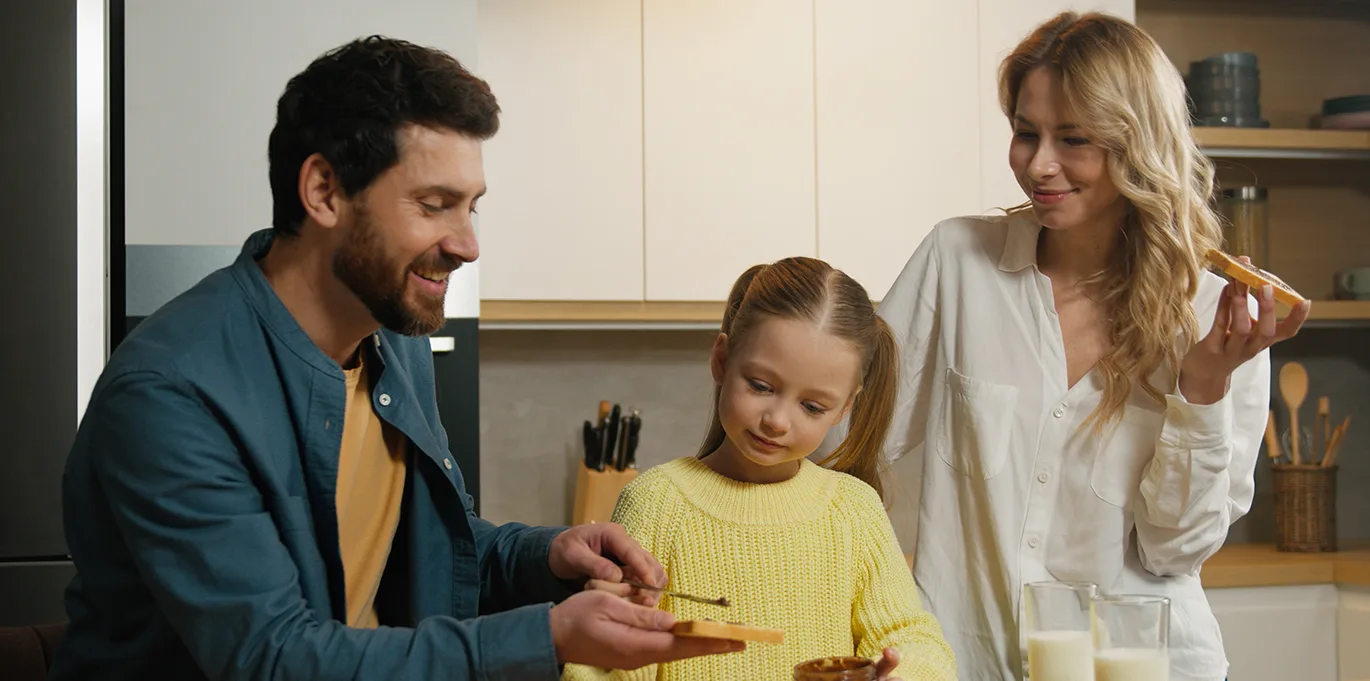 Χαρούμενη οικογένεια τρώει στην κουζίνα του σπιτιού της που είναι εξοπλισμένη με οικιακές μικροσυσκευές.