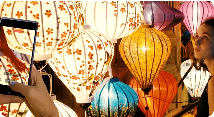 Μία κοπέλα σε σκοτεινό φόντο και φαναράκια στέκεται για φωτογράφιση, ενώ ο χρήστης τραβάει το σκηνικό   